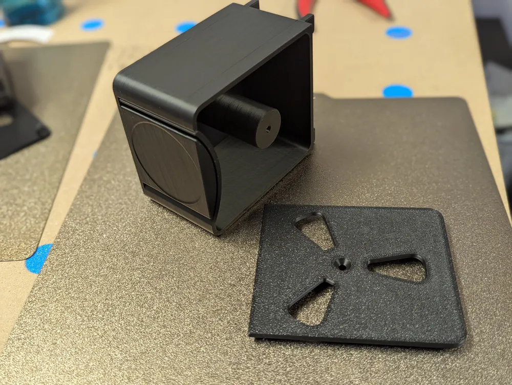 Interior do dispensador de etiquetas impresso em 3D a mostrar o rolo amarelo encaixado no eixo central e os ganchos Skadis.