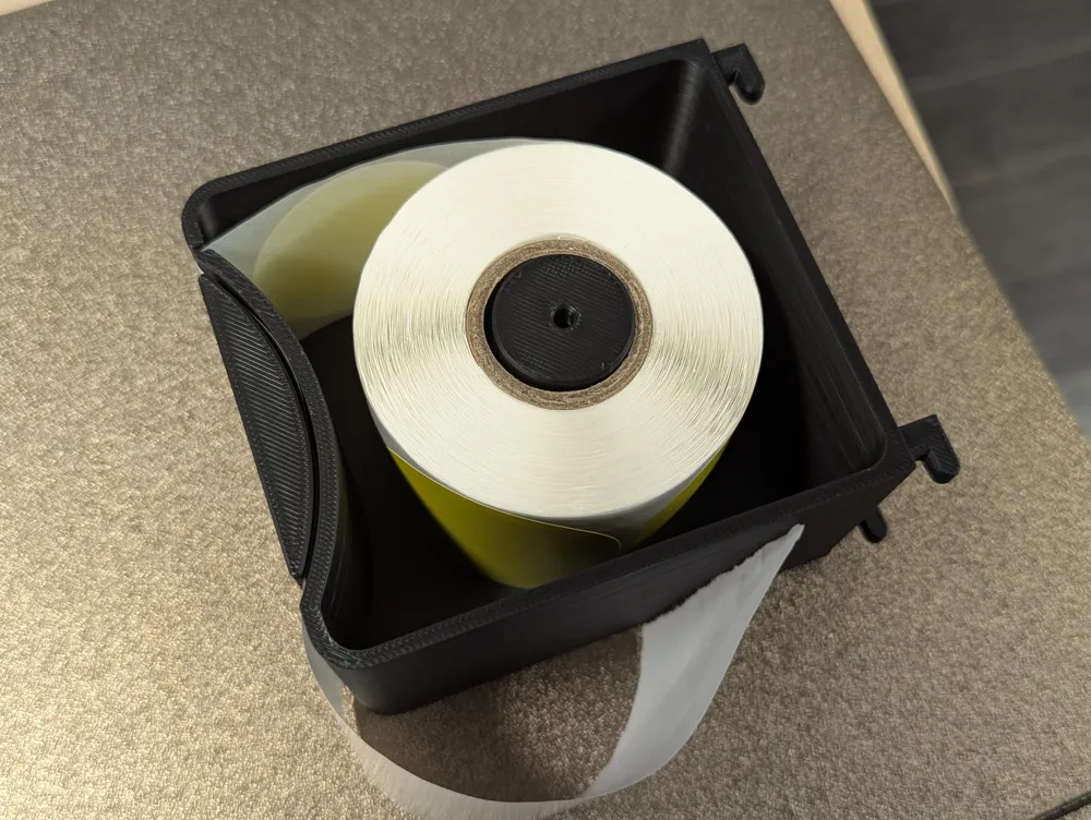 Interior do dispensador de etiquetas impresso em 3D a mostrar o rolo amarelo encaixado no eixo central e os ganchos Skadis.