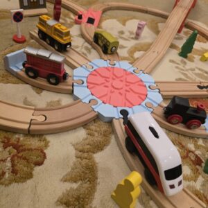 Plataforma giratória preta impressa em 3D, rodando 360 graus, ligada a carris de comboio de madeira no chão.