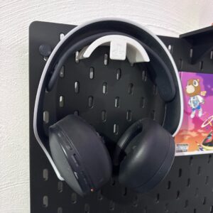 Suporte de auscultadores preto impresso em 3D com logotipo da SteelSeries, montado num painel IKEA Skadis preto, a segurar um headset.