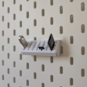 Organizador branco impresso em 3D montado num painel IKEA Skadis branco, segurando adaptadores e cartões de memória SD.