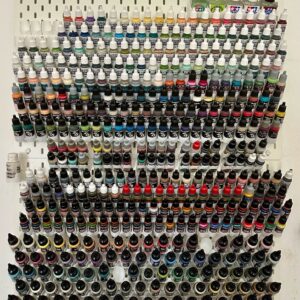 Módulo cinzento impresso em 3D encaixado num painel IKEA Skadis branco, segurando frascos de tinta conta-gotas de forma angular.