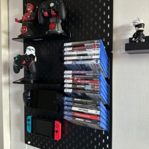 Suporte cinzento escuro impresso em 3D no painel IKEA Skadis, concebido para exibir caixas de videojogos multiplataforma em ângulo.